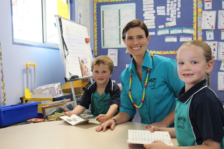 Teacher smiling with two students sitting at a table in the classroom
