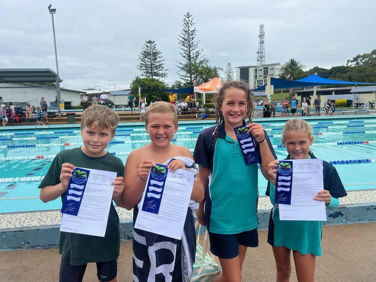 Relay team students smiling holding their ribbons with swimming pool in the background